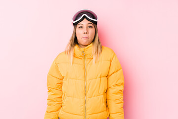 Young caucasian woman wearing a ski clothes in a pink background shrugs shoulders and open eyes confused.
