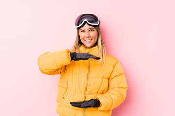 Young caucasian woman wearing a ski clothes in a pink background holding something with both hands, product presentation.