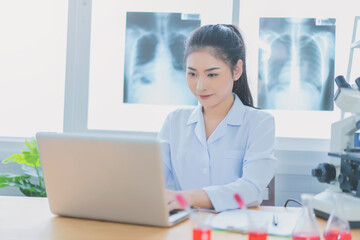 Asian female doctor working on laptop with a microscope for an coronavirus exam at hospital giving patient convenience online service advice,  write a prescription , healthcare, preventing disease