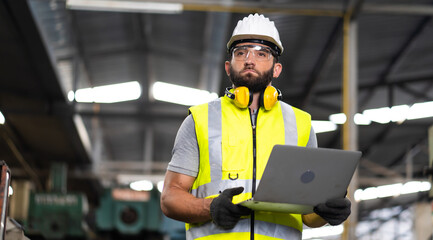 Fototapeta na wymiar Young caucasian engineering man in Hard Hat Wearing Safety Jacket working on laptop computer in Heavy Industry Manufacturing Facility.