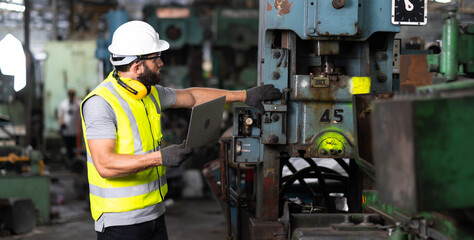 Fototapeta premium Young caucasian engineering man in Hard Hat Wearing Safety Jacket&nbsp;working on laptop computer in Heavy Industry Manufacturing Facility.