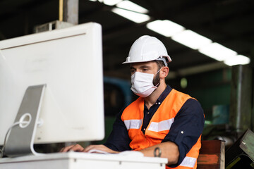 Young caucasian engineering man worker working on digital tablet computer at manufacturing. Worker man wearing face mask prevent covid-19 virus and protective hard hat.