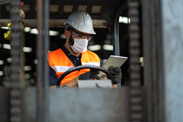 Young male staff driving forklift in warehouse. Worker man wearing face mask prevent covid-19 virus...