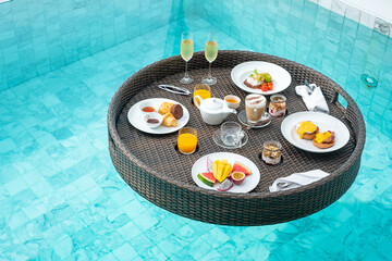 Floating Breakfast tray in swimming pool at luxury hotel or tropical resort villa, fruits; mango, watermelon dragon and passion fruit, food, bread, coffee, tea, wine and orange juice. Exotic summer