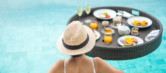 Happy woman in white swimsuit having Floating Breakfast tray in luxury pool hotel, young female with hat enjoy in tropical resort. Relaxing, Exotic summer travel, holiday, vacation and weekend