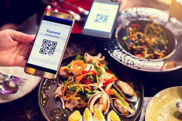 Smartphone in hand to scan QR code payment tag with blurry food and dessert in restaurant to...