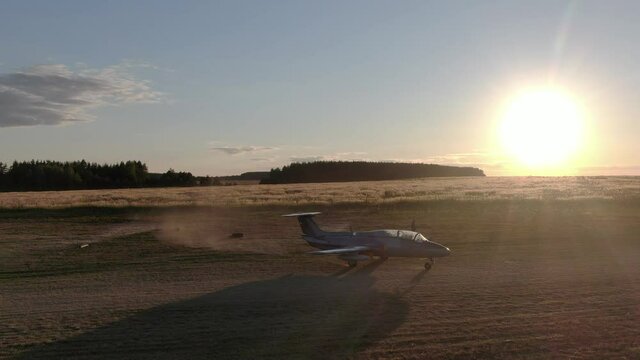 Aero L-29 Delfin Jet plane starting, is about to launch from field, making cloud of dust by turbine engine against sunset light, aerial shot