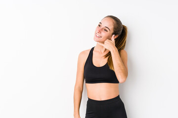 Young caucasian fitness woman posing in a white background showing a mobile phone call gesture with fingers.