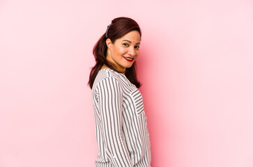 Middle age latin woman isolated on a pink background looks aside smiling, cheerful and pleasant.