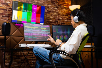 asian male media content creator editing video footage on computer in home studio. post production,...