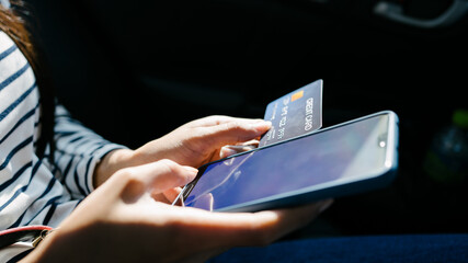 Young asian woman sitting at backseat of car and using mobile and holding credit card in hands.