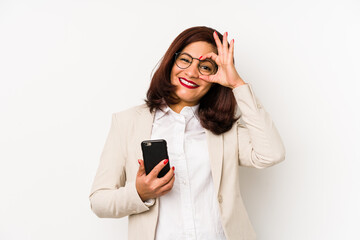 Middle age latin woman holding a mobile phone isolated excited keeping ok gesture on eye.