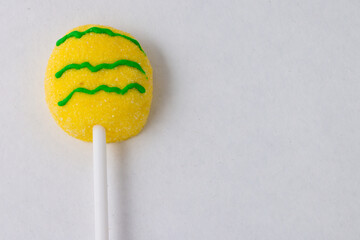 Easter Egg candy, bright yellow and green squiggles, on lollipop stick on white.