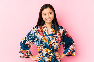 Young chinese woman wearing a kimono pajama isolated confident keeping hands on hips.