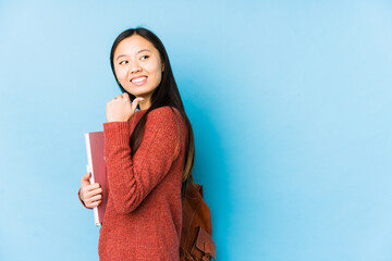 Young chinese student woman isolated points with thumb finger away, laughing and carefree.