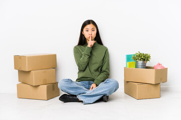 Young chinese woman moving to a new home keeping a secret or asking for silence.