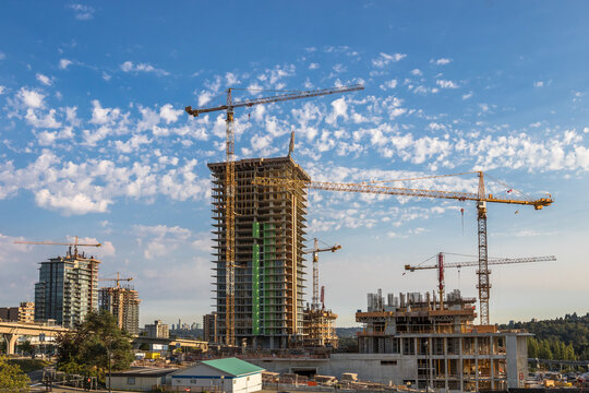New construction of high-rise buildings in Coquitlam City, industrial construction site, construction equipment, several construction cranes on the background of finished skyscrapers and a blue cloudy
