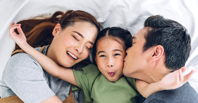 Top view of portrait enjoy happy smiling love asian family father and mother with young parents little asian girl looking at camera in moments good time lying on the floor at home