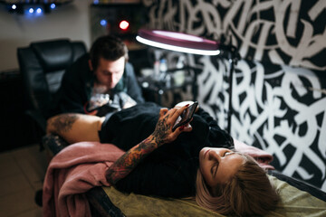 
the girl uses the phone in search of news at that moment she gets a tattoo on her leg in the salon