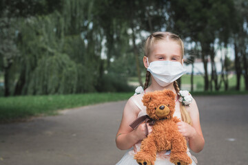 little girl in a protective mask and a teddy bear in her hands
