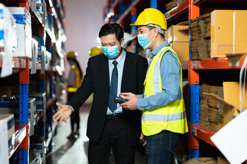 Management visits and inspects the work request for employees in the warehouse. Worker man wearing face mask prevent covid-19 virus and protective hard hat.