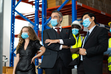 Warehouse managers and worker wearing face mask prevent covid-19 virus and protective hard hat and working together in warehouse workplace. Professional engineering team.