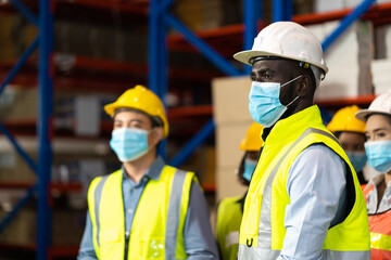 Warehouse worker in protective medical face mask working at large warehouse.  Many employees are working intently in the warehouse. Diversity peoples at work.