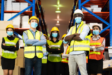 Warehouse worker in protective medical face mask working at large warehouse.  Many employees are working intently in the warehouse. Diversity peoples at work.