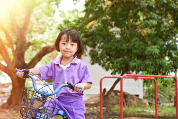 Beautiful smiling little girl riding bicycle in a park on sunny day outdoor.