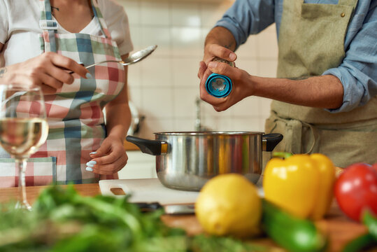 Cropped Shot Of Man Adding Pepper, Spice To The Soup While Woman Holding A Spoon. Couple Preparing A Meal Together In The Kitchen. Cooking At Home, Italian Cuisine