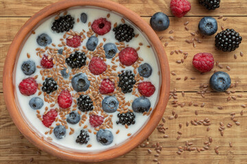 Yogurt with blueberries, raspberries, blackberries, flax seeds in a clay bowl. Served vegetarian dish. Healthy breakfast, healthy food. Background for the menu of restaurants, cafes.
