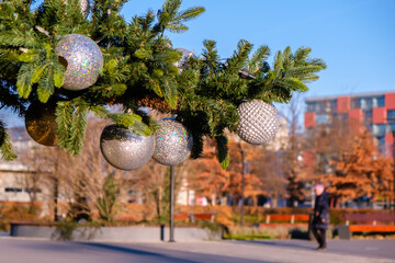 Branch of artificial Christmas tree with white christmas balls on city street outdoors at sunny summer day.