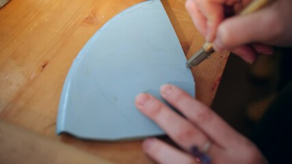 Female hands carefully cutting piece of ceramic with glass cutter. Close up - Powered by Adobe