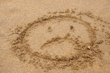 Fototapeta na wymiar Unhappy face sign on a yellow sand. Concept state of mind