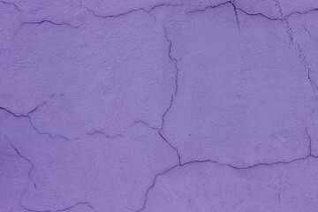 The texture of cracked lavender plaster. The old purple wall is covered with dilapidated, uneven plaster. Texture of vintage purple wall surface, closeup. Blank for design