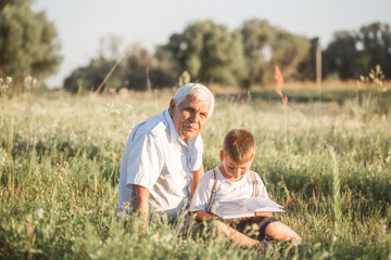 Mid shot of grandfather and his grandson while reading a book together in meadow Small boy making first steps in read.