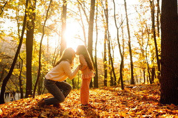 Stylish young Mother and daughter walking in the autumn forest at sunset. Mother and daughter embrace in autumn park. Mom and child having fun together in autumn. Family on a walk. 