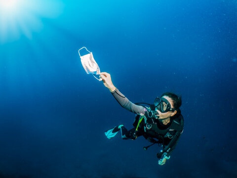 Concept Of Sea Pollution With A Scuba Diver Who Picks Up A Used Face Mask Underwater