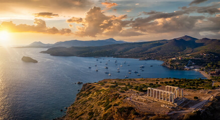 Panorama des Kap Sounion bei Athen zum Sonnenuntergang mit Tempel des Poseidon und zahlreichen Segelbooten vor Anker in der Bucht, Attika, Griechenland