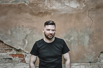 Charming handsome. Bearded sexy young man a stylish hairstyle in a fashionable black t-shirt near the old  wall.