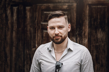 Portrait of a successful young businessman. Young beautiful fashionable hipster guy walking down near wooden doors.