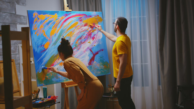 Man and woman painters working together in art studio on large canvas.