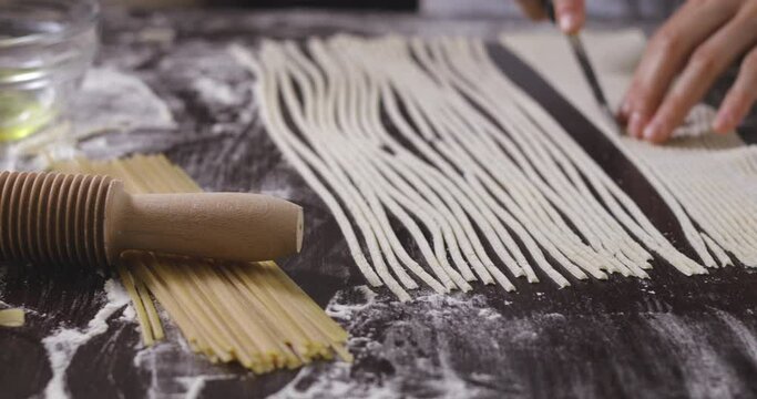 Making pasta by cutting dough with rolling pin. Traditional Italian way of making homemade spaghetti or tagliatelle.