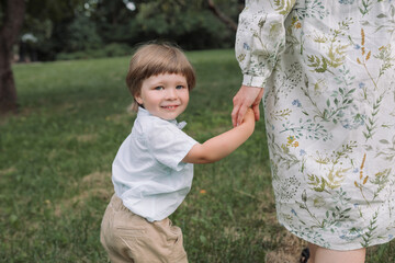 Pretty little boy holding his mother while walking in the park.