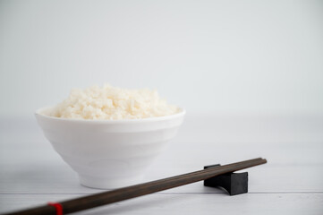Thai steamed rice in a bowl with a spoon and black chopsticks placed on the side. On a white backdrop