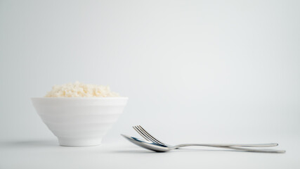 Thai steamed rice in a bowl with a spoon and black chopsticks placed on the side. On a white backdrop