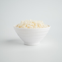Thai steamed rice in a bowl with a spoon and black chopsticks placed on the side. On a white backdrop