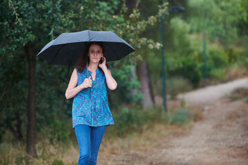 woman walking in the rain with black umbrella in rural setting