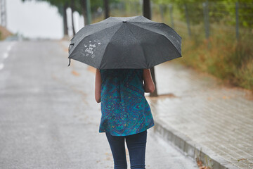 woman walking in the rain with black umbrella in rural setting