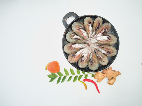 Top view of fresh prawns on a black plate,along with tomato, ginger and curry leaves selective focus.white background.